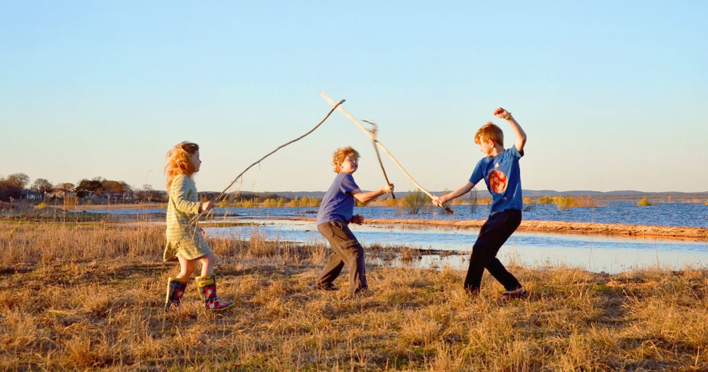 3 kids playing swordfighting with sticks